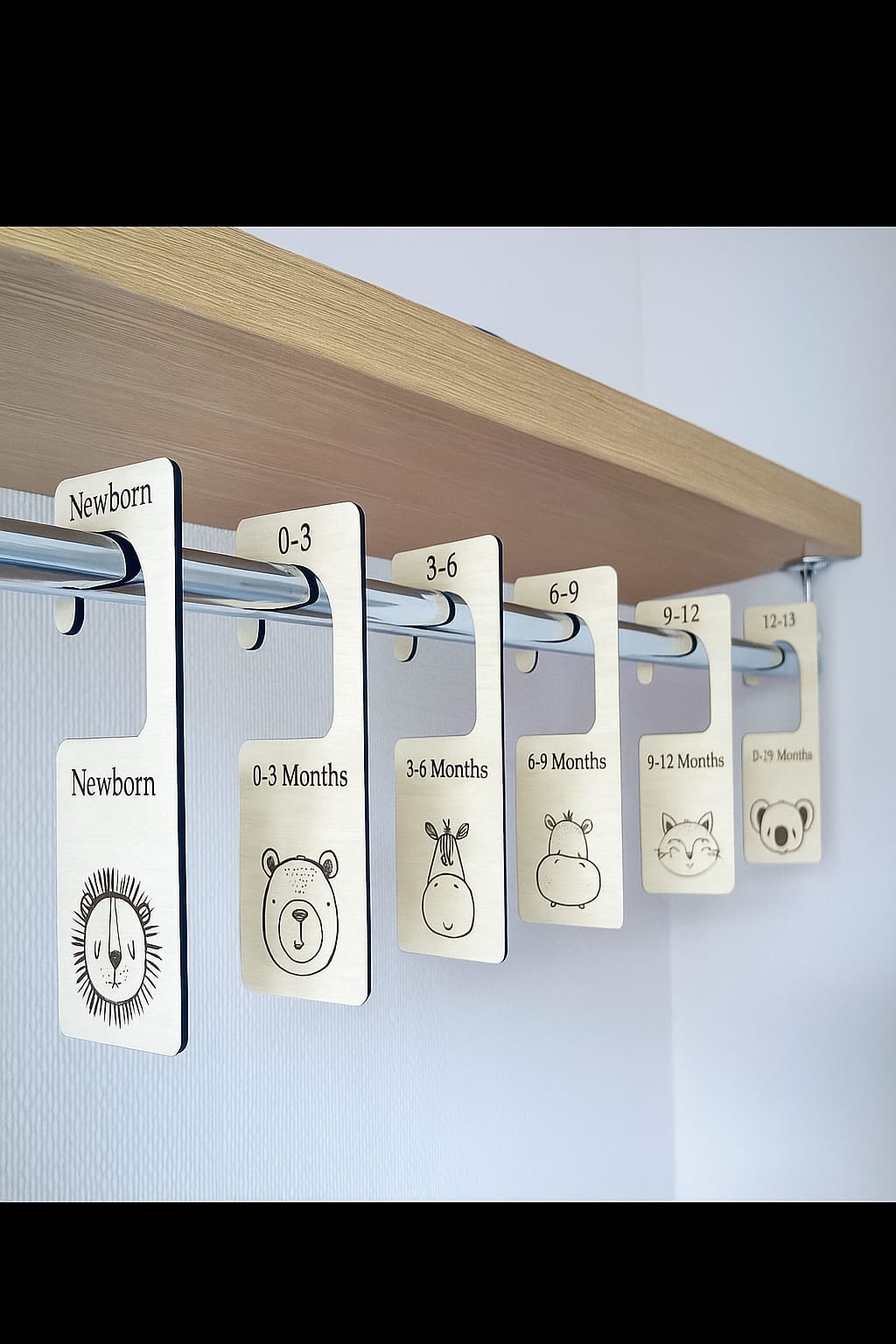 Clothing size tags labeled from Newborn to 24 Months on a wooden shelf.