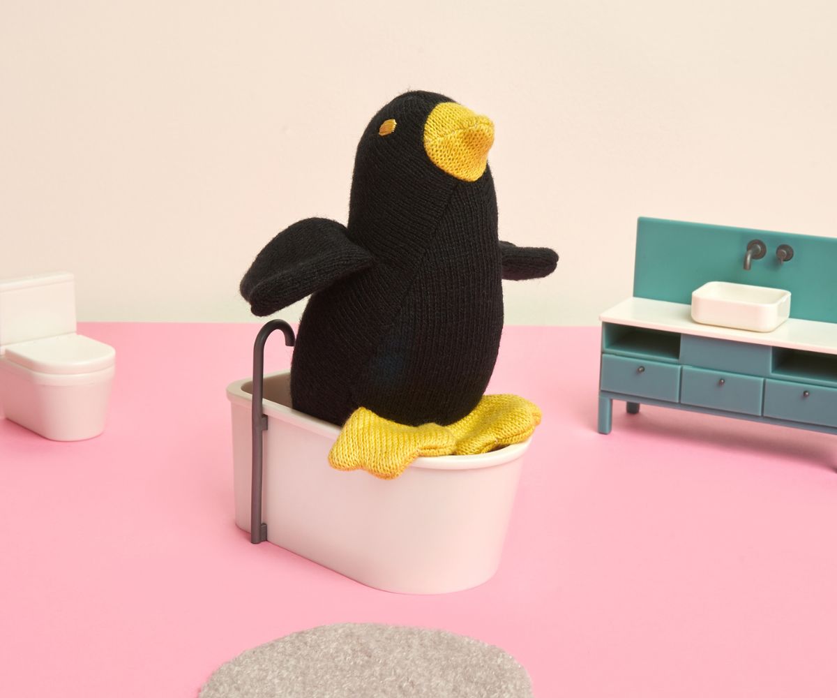 A small black organic cotton toy in the shape of a blackbird with yellow feet and a soft body, designed for sensory development.