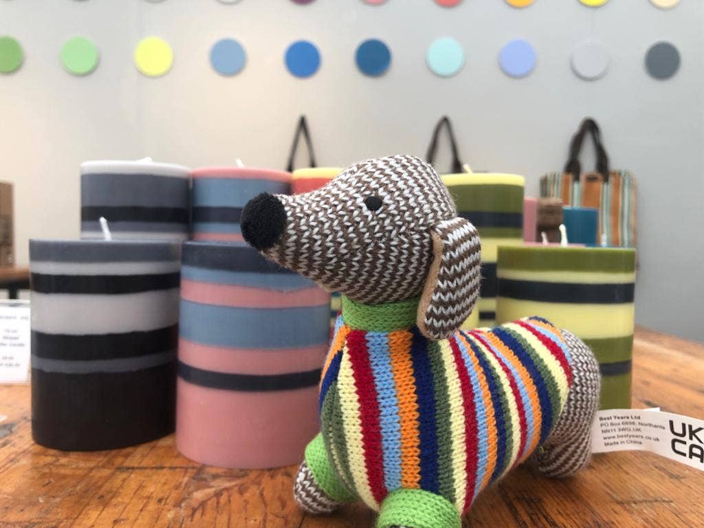Knitted dog toy with colorful stripes on a wooden table with striped candles and polka dot wall in the background.