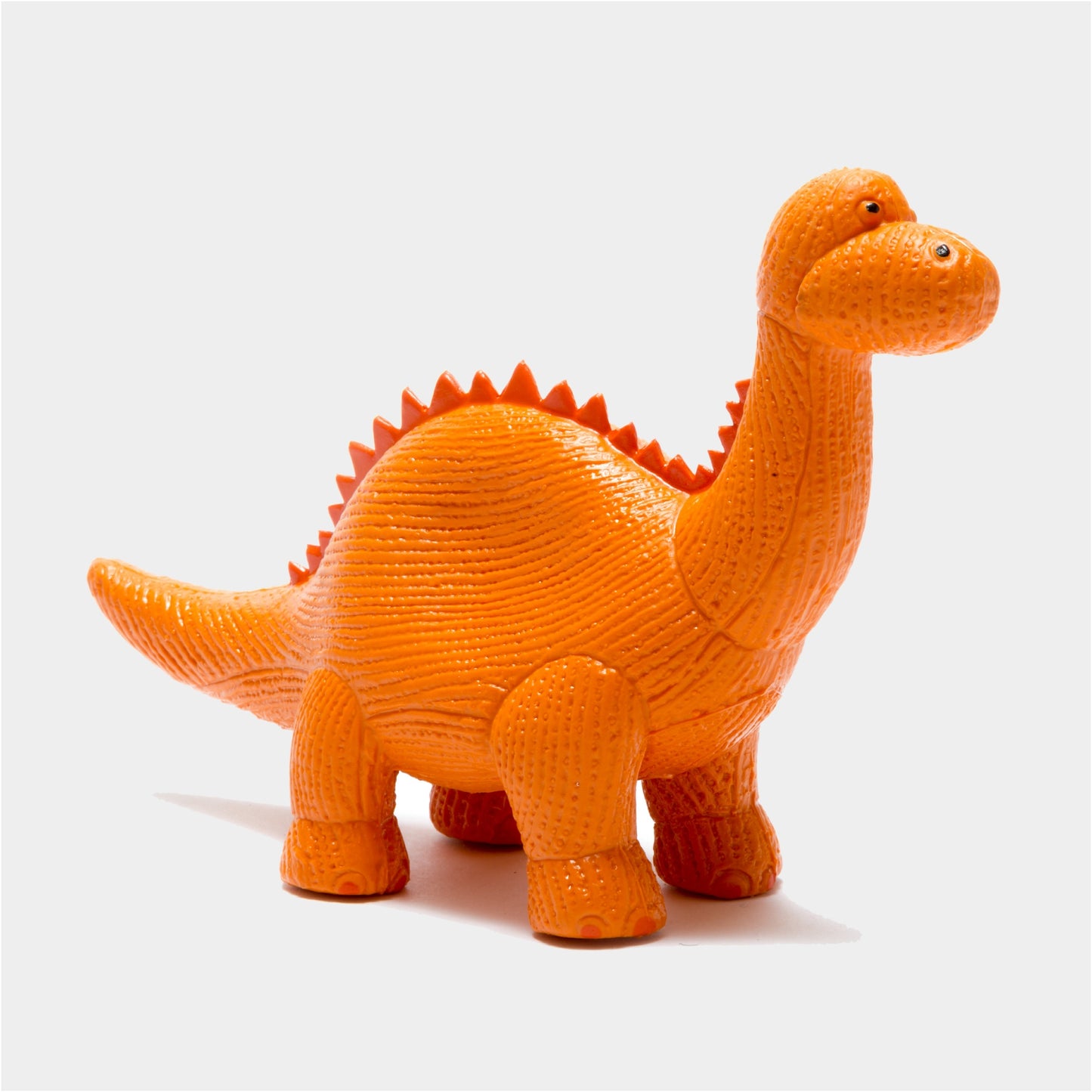 An orange textured dinosaur toy, resembling a long-necked sauropod with a spiked back, standing on a light gray background.