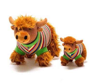 Two plush toys resembling Highland cows wearing colorful sweaters on a white background