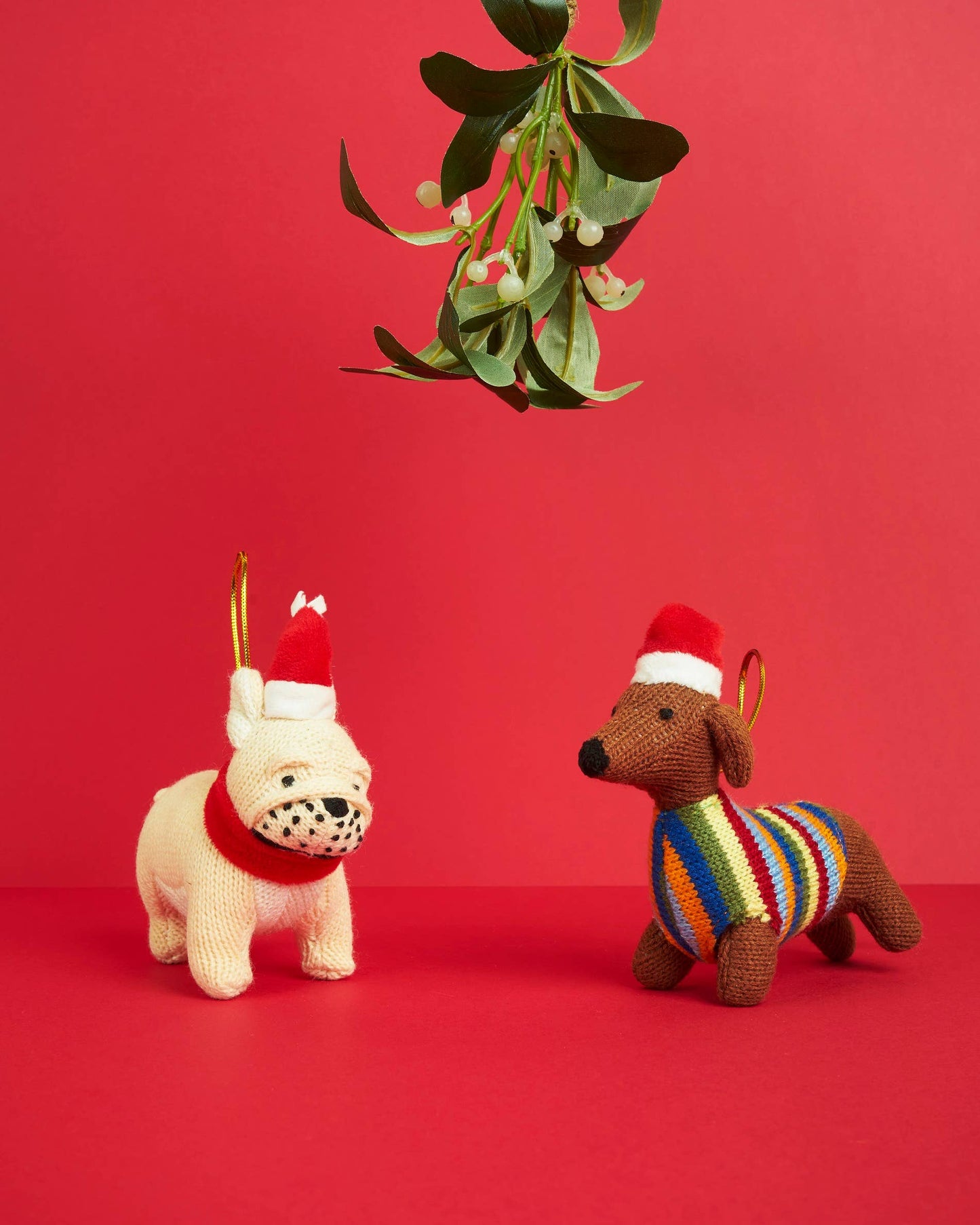 Two knitted dog toys on a red background with mistletoe.
