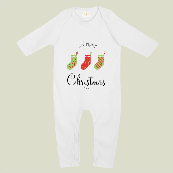 A white long-sleeve baby bodysuit with a festive graphic on the chest reading 'MY FIRST Christmas' and three Christmas stockings, shown against a solid light sage green background.
