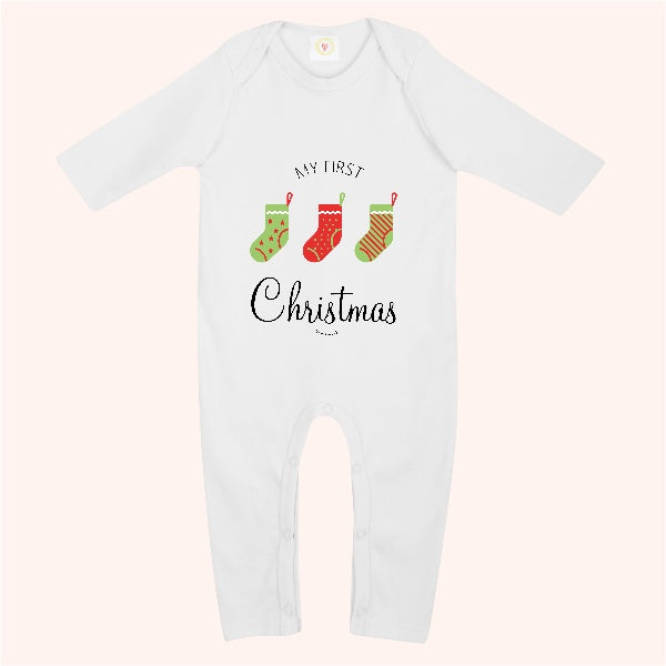 A white long-sleeve baby bodysuit with a festive graphic on the chest reading 'MY FIRST Christmas'. The graphic features three Christmas stockings in green, red, and orange with stripes, set against a pale pink background.
