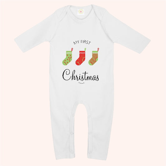 A white long-sleeve baby bodysuit with a festive graphic on the chest reading 'MY FIRST Christmas'. The graphic features three Christmas stockings in green, red, and orange with stripes, set against a pale pink background.