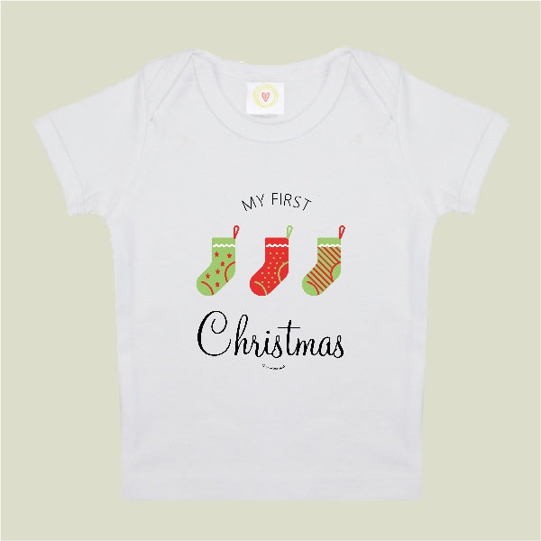 White baby onesie with 'My First Christmas' text and stockings on a beige background