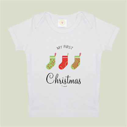 White baby onesie with 'My First Christmas' text and stockings on a beige background