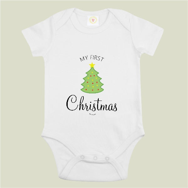 A white short-sleeve baby bodysuit with a graphic print of a green Christmas tree and the text 'MY FIRST Christmas' on a light beige background.