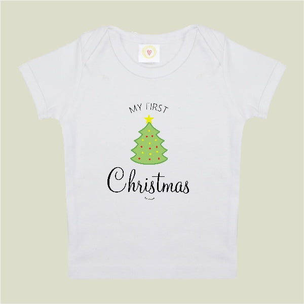 A white short-sleeve baby t-shirt with a graphic print of a green Christmas tree and the text 'MY FIRST Christmas' on a light beige background.