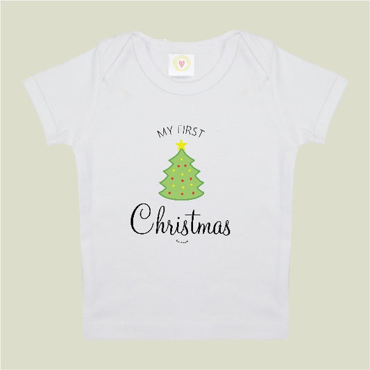 A white short-sleeve baby t-shirt with a graphic print of a green Christmas tree and the text 'MY FIRST Christmas' on a light beige background.