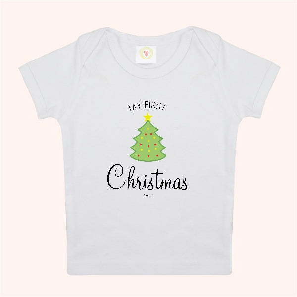 A white short-sleeve baby t-shirt with a graphic print of a green Christmas tree and the text 'MY FIRST Christmas' on a light pink background.