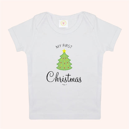A white short-sleeve baby t-shirt with a graphic print of a green Christmas tree and the text 'MY FIRST Christmas' on a light pink background.