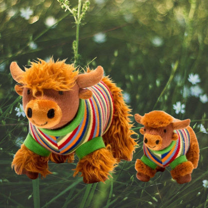 Two plush cow toys wearing colorful sweaters in a grassy outdoor setting