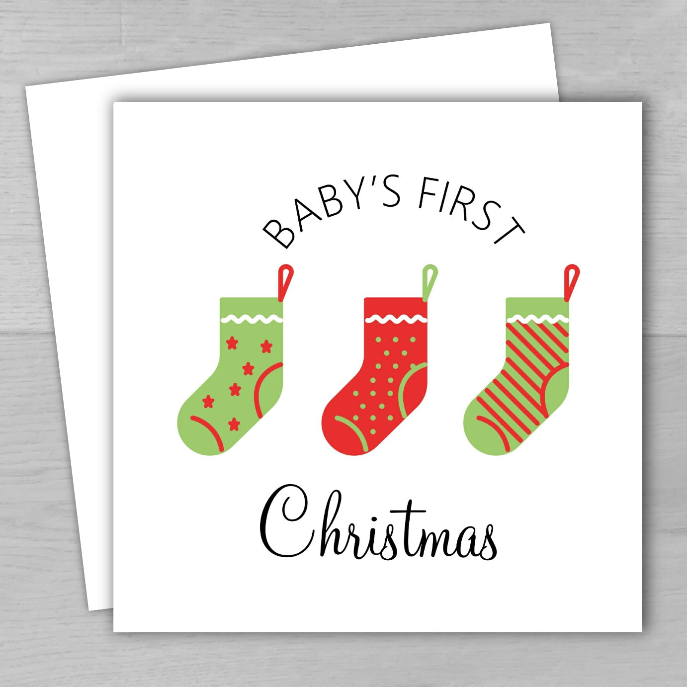 Card with red and green Christmas stockings and 'Baby's First Christmas' text on a white background.