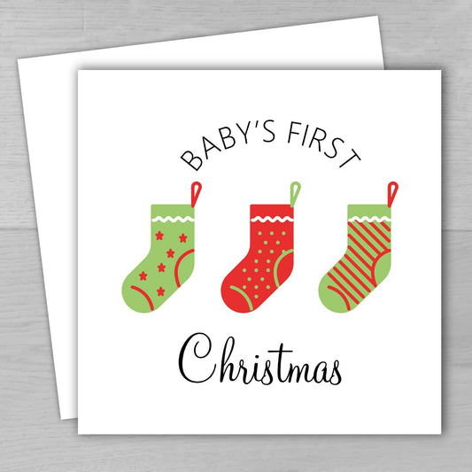 Card with red and green Christmas stockings and 'Baby's First Christmas' text on a white background.